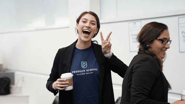 A smiling woman in a "Product School Silicon Valley" T-shirt holds a coffee cup and flashes a peace sign, embodying employee empowerment; another woman beside her laughs, both enjoying a bright indoor setting. | Humanico Workforce Intelligence Software