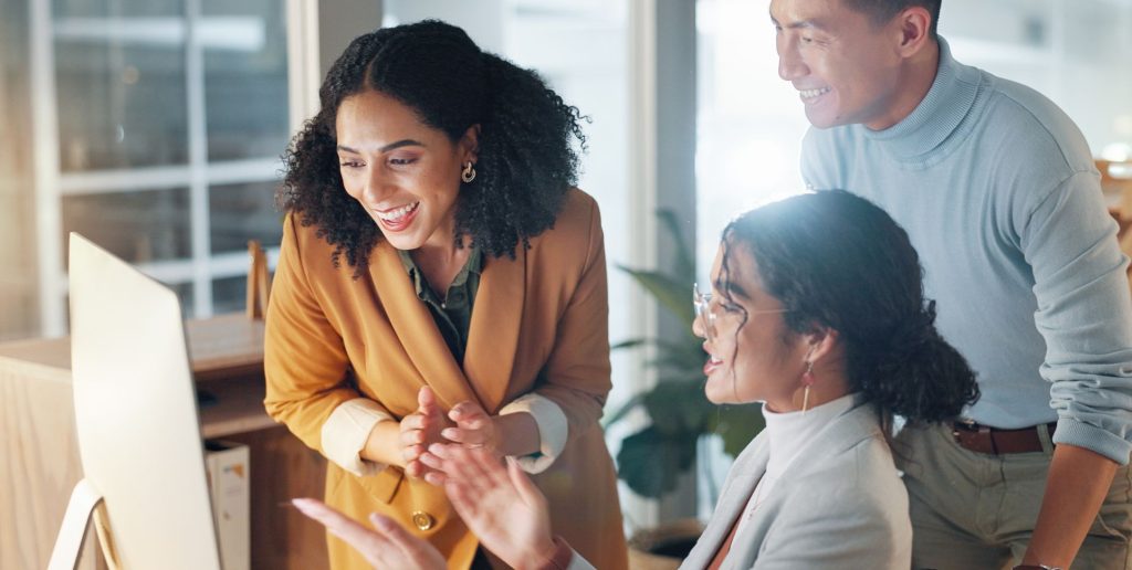 Three colleagues smile and look at a computer screen together in a modern office, appearing engaged and enthusiastic as they explore HR tools for new managers during an onboarding session. | Humanico Workforce Intelligence Software