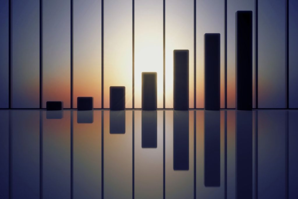 A bar graph with vertical bars of increasing height, symbolizing employee retention, is shown against a sunset or sunrise background, with the bars and sky reflected on a shiny surface below. | Humanico Workforce Intelligence Software