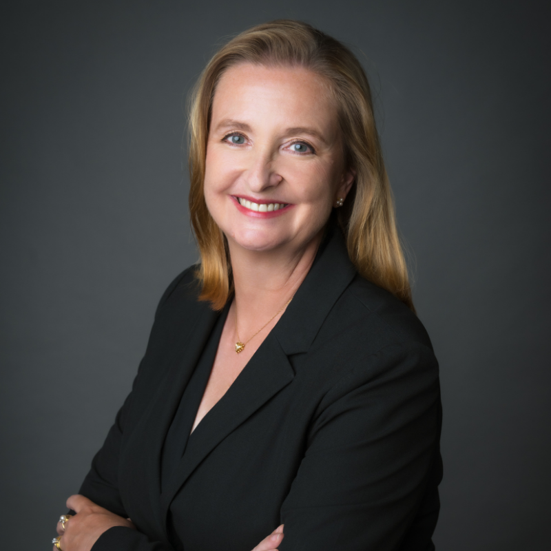 Rachael Fitzpatrick, with shoulder-length blonde hair, wearing a black blazer and gold necklace, smiles confidently with arms crossed against a dark gray background. | Humanico Workforce Intelligence Software