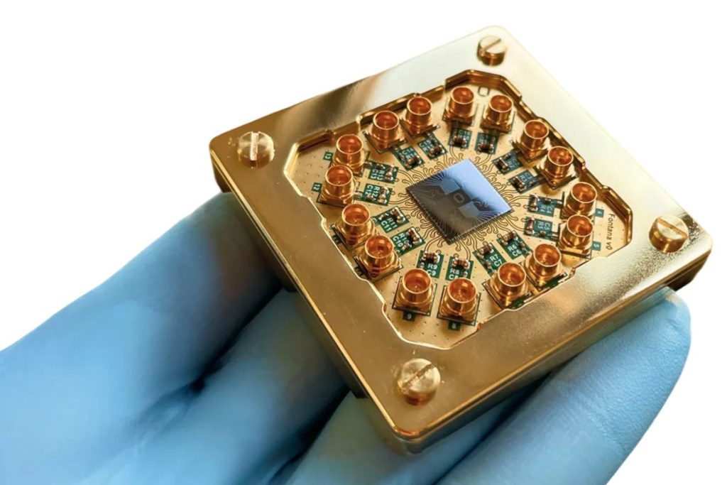 A gloved hand holds a gold-colored quantum computer chip with multiple connectors and a central black square component, highlighting innovation that goes beyond qualifications, set against a white background. | Humanico Workforce Intelligence Software