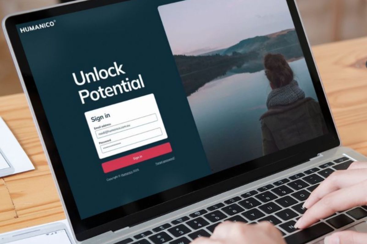 A person types on a laptop displaying the "HUMANICO" sign-in page with the message "Unlock Potential," showcasing HR software Australia and tools for new managers, and an image of someone looking at a lake and hills in the background. | Humanico Workforce Intelligence Software