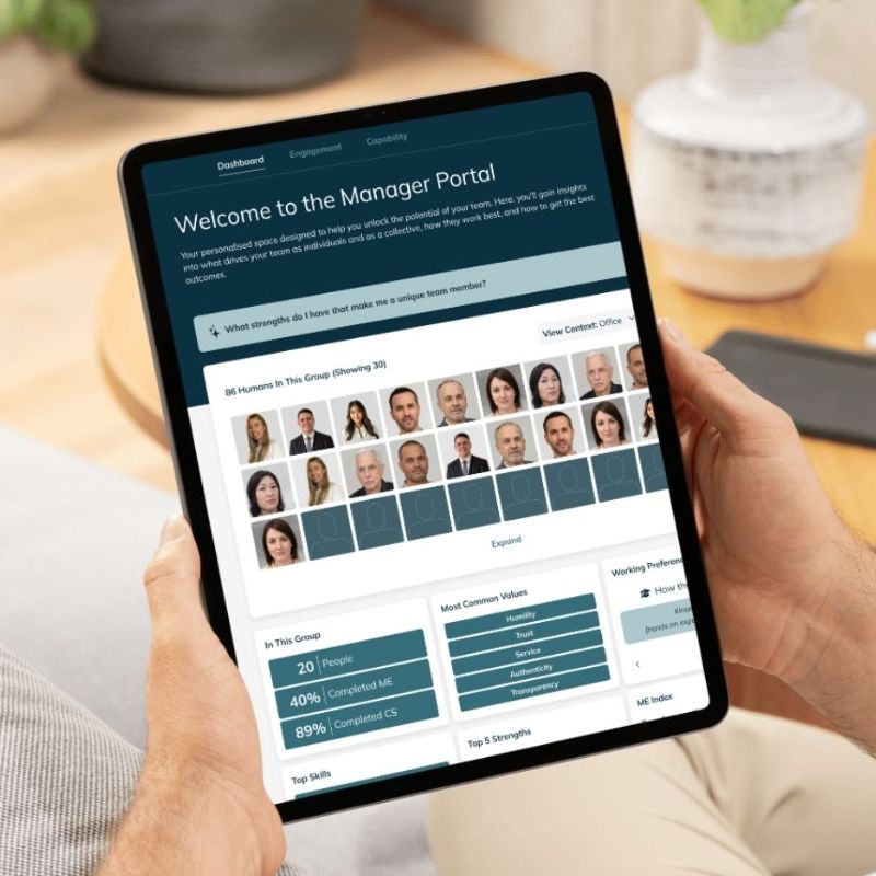A person holds a tablet displaying a manager portal dashboard—an essential HR tool for new managers—with group statistics, charts, and employee headshots showcasing data on team size, skill percentages, and onboarding progress in a grid layout. | Humanico Workforce Intelligence Software